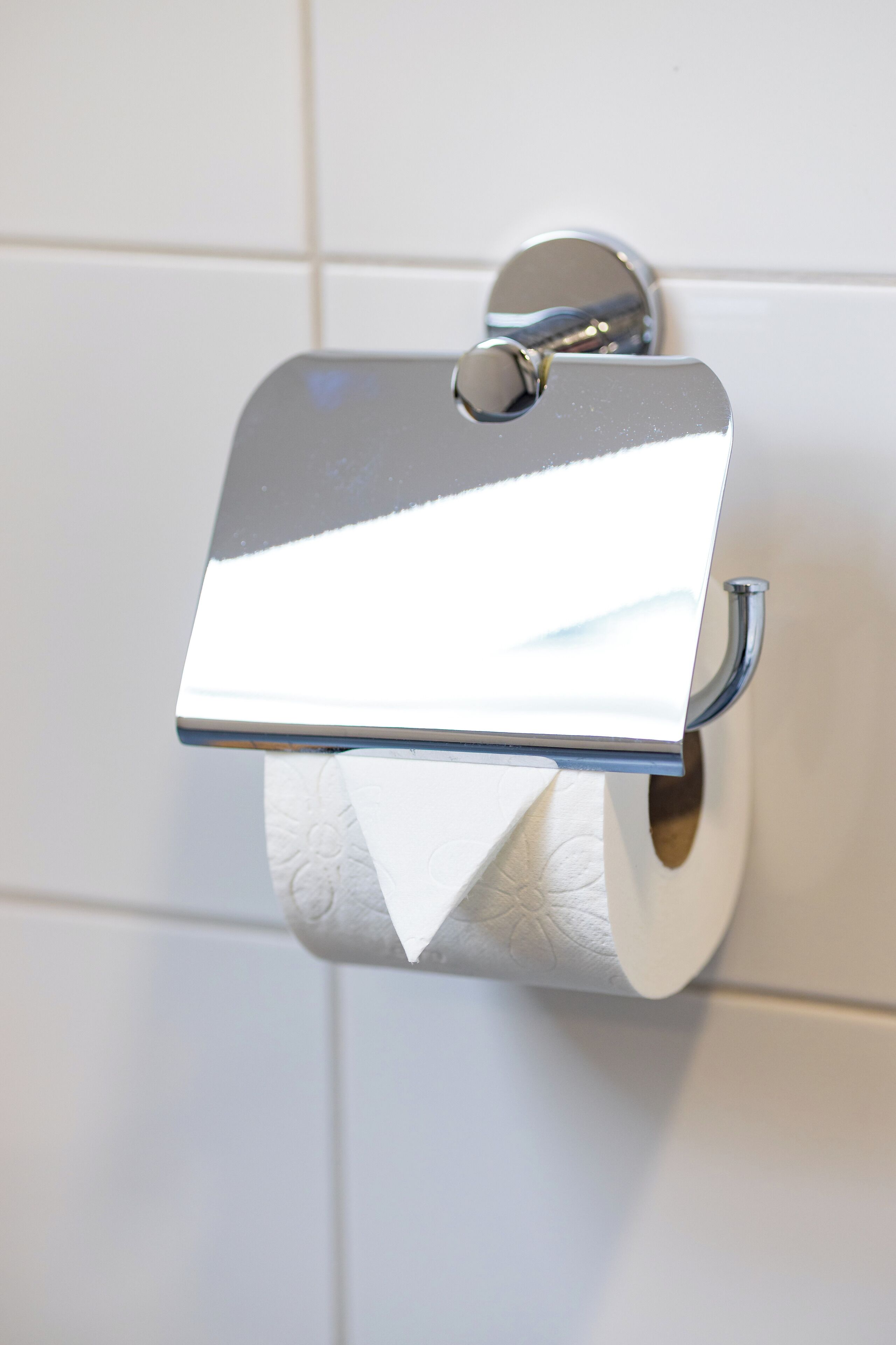 A toilet paper holder with a metallic lid and a roll of toilet paper.