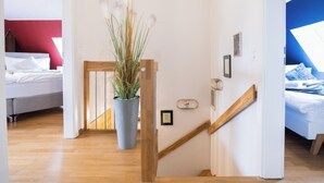 A modern hotel room with a wooden staircase, a large potted plant, and a bed with white bedding. - Duplex Apartment – Lake Constance – Self-Check-In – Parking – 4-Keys Apartments (Rorschach)