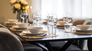 A dining table set with white bowls, plates, and glasses, with a vase of flowers in the background. - Duplex Apartment – Lake Constance – Self-Check-In – Parking – 4-Keys Apartments (Rorschach)