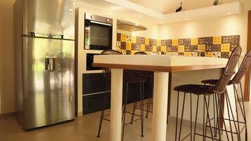 A compact kitchen with a stainless steel refrigerator, a built-in oven, and a tiled backsplash.