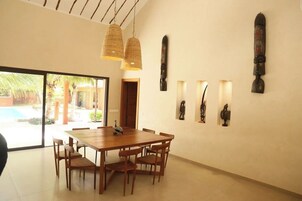 Un comedor espacioso con una mesa y sillas de madera, ventanas amplias y esculturas en la pared.