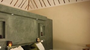 Ένα υπνοδωμάτιο με ένα κρεβάτι, έναν ανεμιστήρα οροφής και έναν τοίχο με ανάγλυφη υφή.