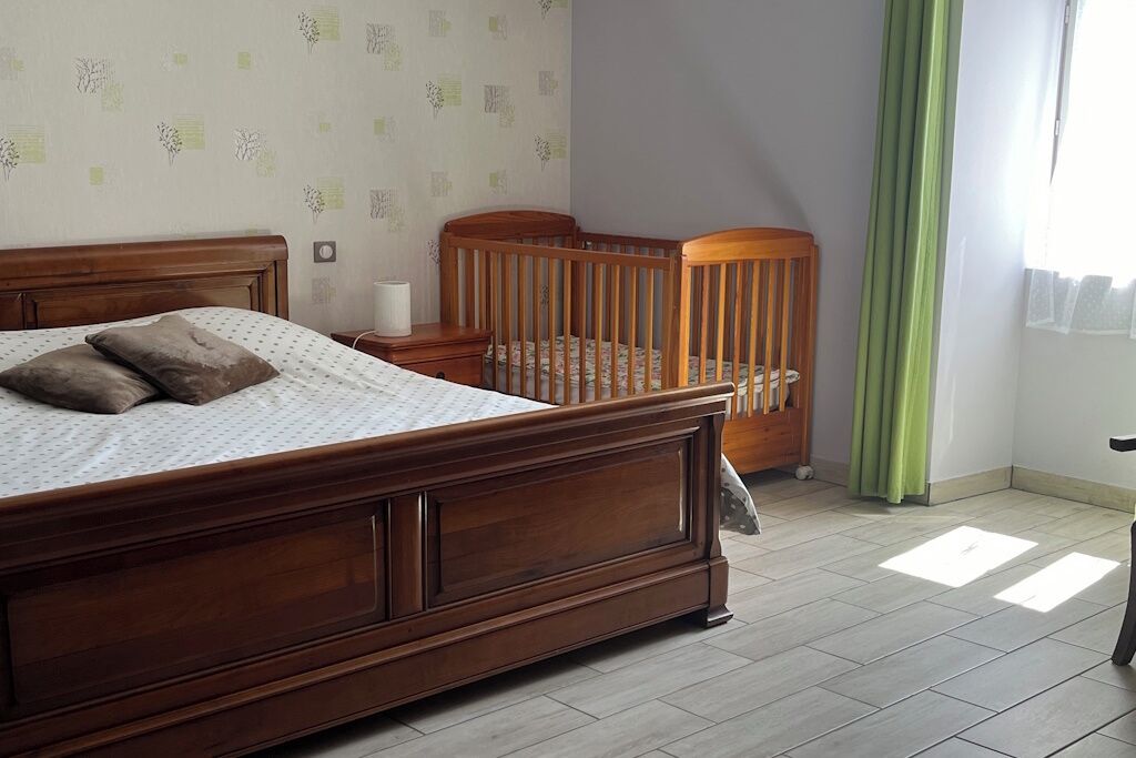 Een slaapkamer met een houten bed, een ledikant, een nachtkastje en een raam met gordijnen.