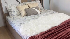 A bed with a floral bedspread, two pillows, a white fluffy blanket, and a red velvet throw. - PPplace Mahidol (Chiang Mai)