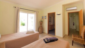 Habitación de hotel con dos camas, un florero grande y una silla de mimbre.