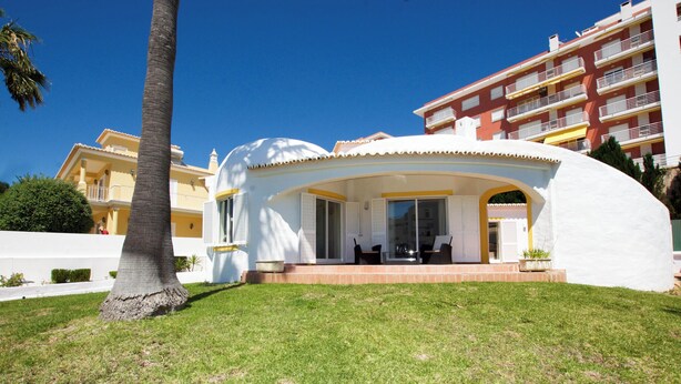 Un edificio blanco con techo curvo y balcón, rodeado de un césped cuidado y una palmera.