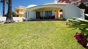 Una villa moderna con techo curvo, un patio con mobiliario exterior y un césped bien cuidado.