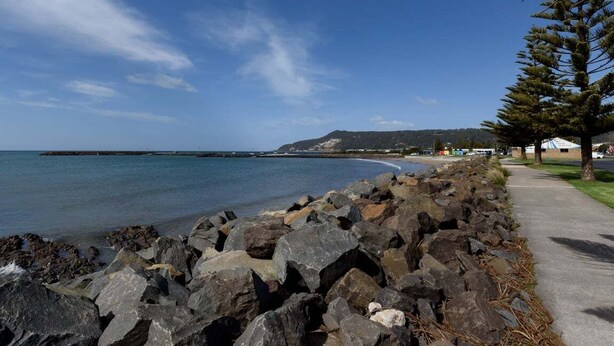 A coastal walkway with large rocks, a clear sky, and a distant view of a beach and hills. - Steps From The Hospital in Burnie (Burnie City)