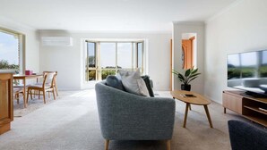 A modern living room with a grey sofa, a wooden coffee table, a TV stand, and a dining area with a table and chairs. - Steps From The Hospital in Burnie (Burnie City)