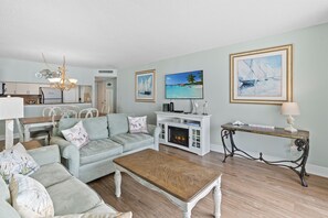 A living room with a sofa, coffee table, and fireplace. There are framed pictures on the wall and a dining area in the background. - S Hampton 1406 3 Br Oceanview in Kingston, Pool (Myrtle Beach)