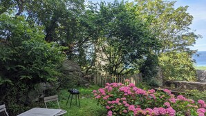 Un jardín con una mesa, sillas, una cerca de madera y flores rosadas.