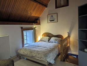 A bedroom with a wooden ceiling, a bed with floral bedding, a window, and a framed picture on the wall. - Mill for 2, facing the sea, 300m to the beach and great walks. Next to a castle. (La Hague)