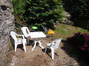 An outdoor seating area with a table and four chairs, surrounded by greenery and a stone wall. - Mill for 2, facing the sea, 300m to the beach and great walks. Next to a castle. (La Hague)