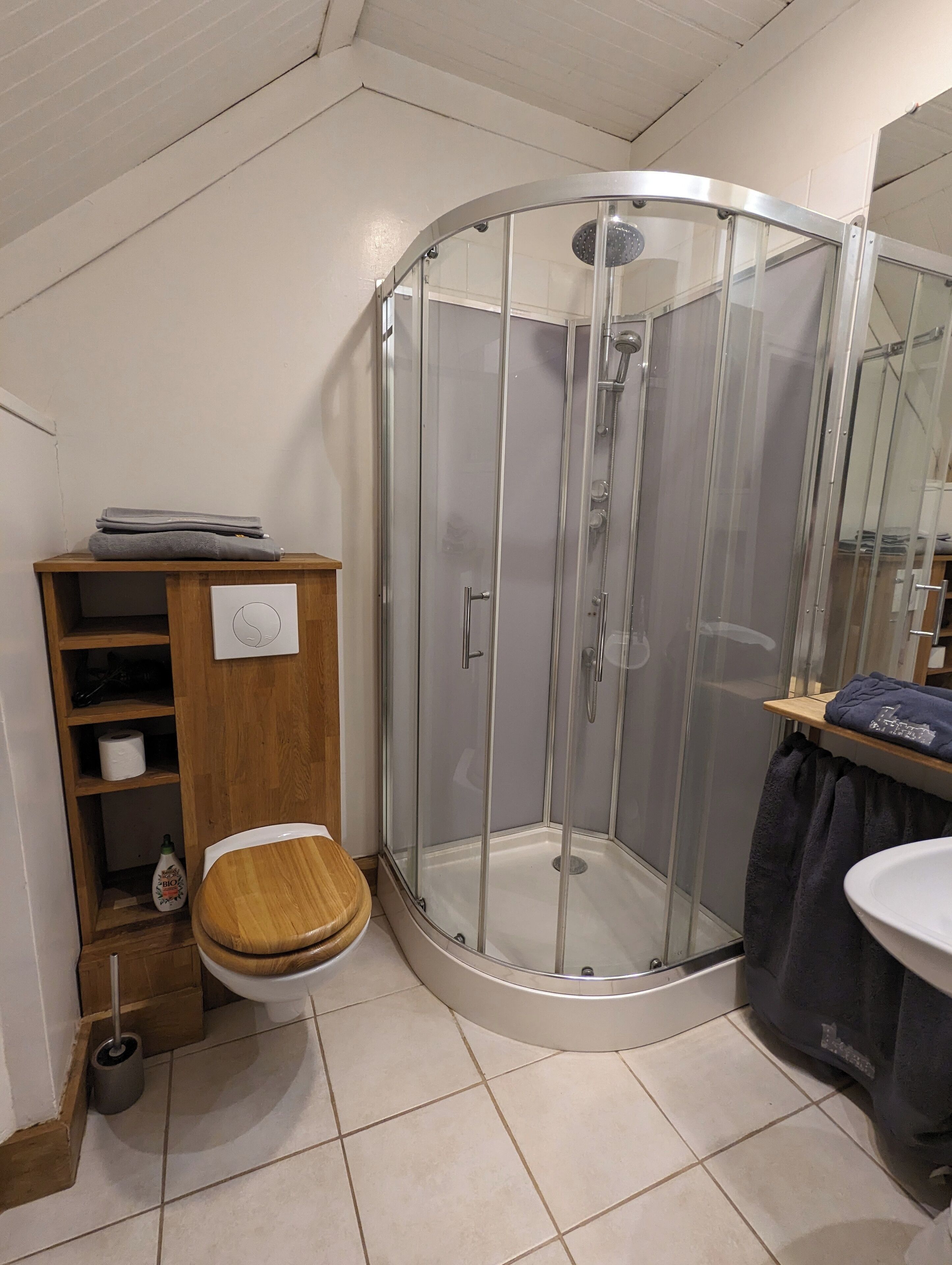 Een badkamer met een douchecabine van glas, een houten toilet en een wastafel met een donkere handdoek.