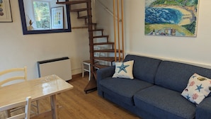Un salón acogedor con un sofá azul, una escalera de madera y un cuadro de una escena costera.