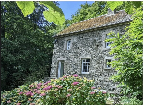 A stone building with a traditional design, surrounded by lush greenery and flowering plants. - Mill for 2, facing the sea, 300m to the beach and great walks. Next to a castle. (La Hague)