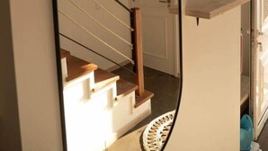 Un espejo con una bombilla colgando del techo, una escalera y un pequeño estante en la pared.