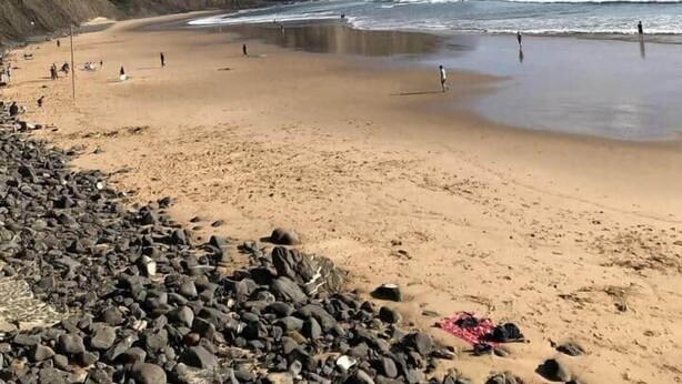 Una playa con primer plano rocoso, una orilla arenosa y acantilados al fondo.