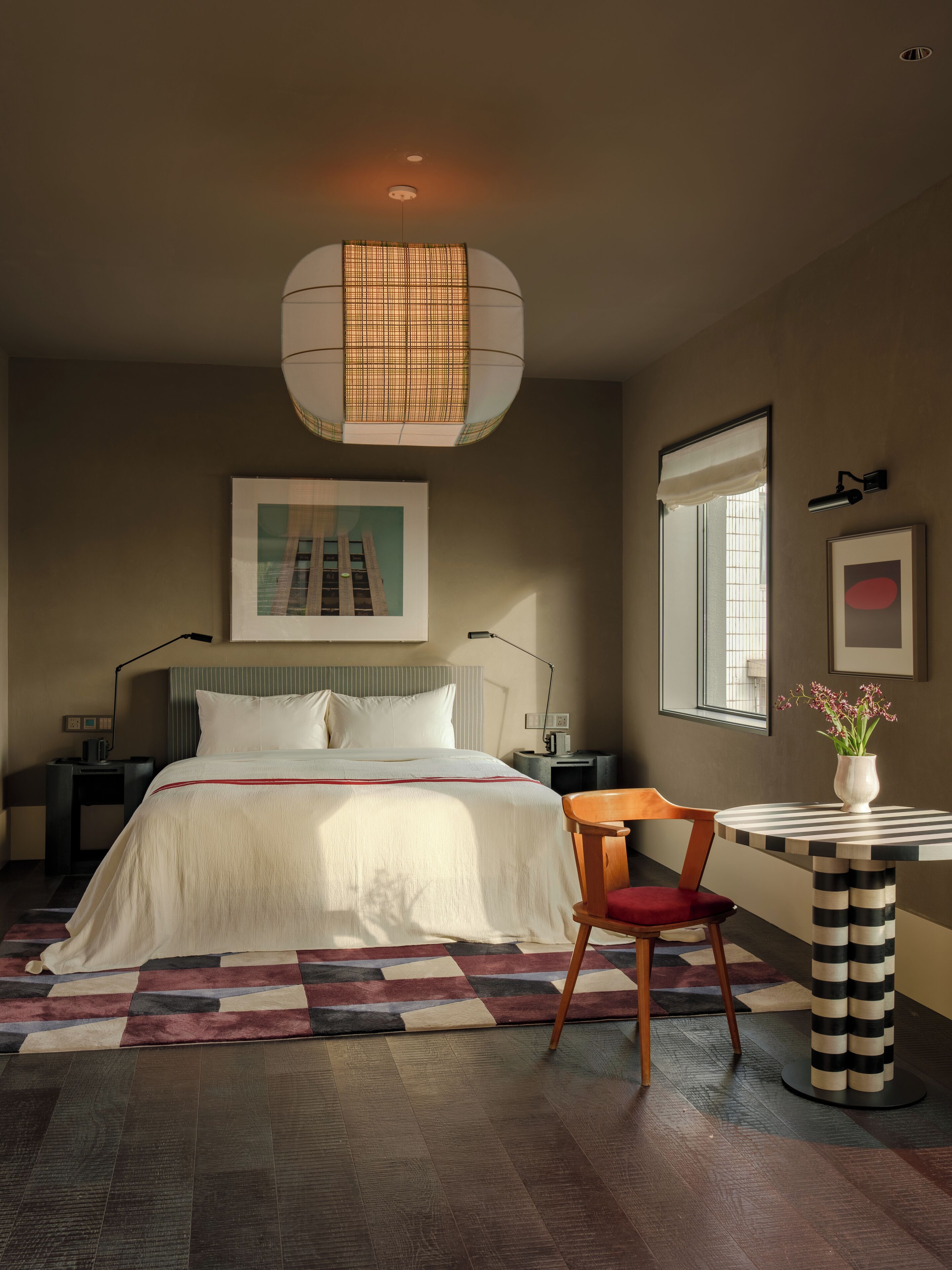 A modern bedroom with a large bed, a chair, a small table, and a hanging light fixture.