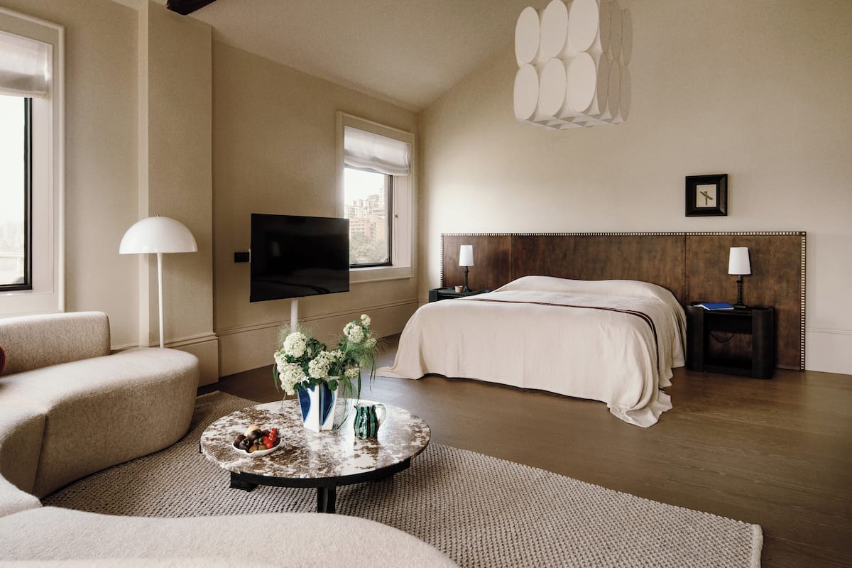 Hotelkamer met een groot bed, een flatscreen televisie, een bank, een bijzettafeltje met bloemen en uitzicht op de stad.