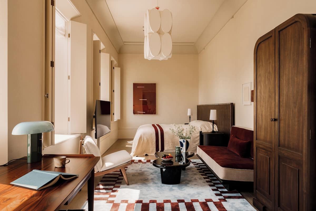 Een hotelkamer met een bed, een bureau met lamp, een bank, een salontafel met vaas en een kledingkast.