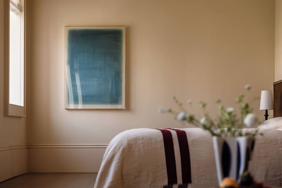 Hotelkamer met een groot abstract schilderij aan de muur, een nachtkastje met een bloevas en een lamp.