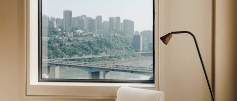 A room with a large window, a chair, a small table with a teapot and cup, and a floor lamp.
