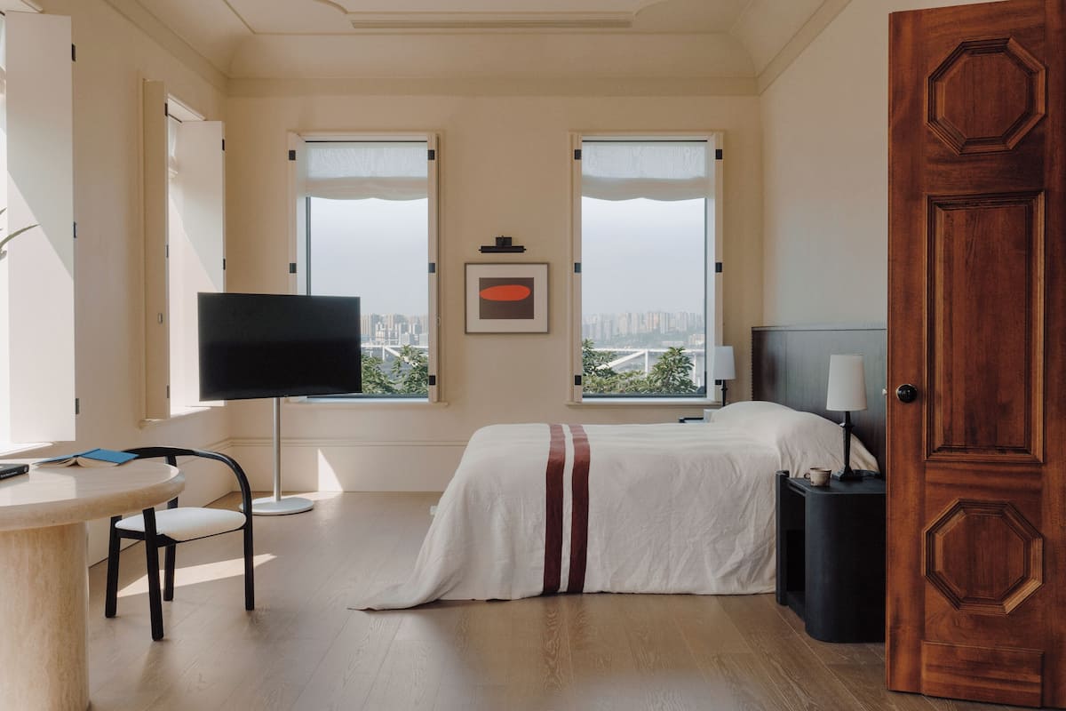 Een hotelkamer met een bed, een bureau, een stoel, een televisie en uitzicht op de stad.