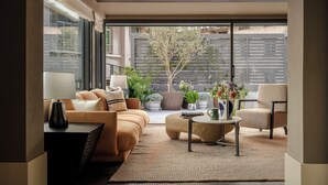 A modern living room with a sofa, armchair, and coffee table, a potted plant, and a view of a tree and fence through large windows. - Sunyata Mountain Alley Chongqing Resort (Chongqing)