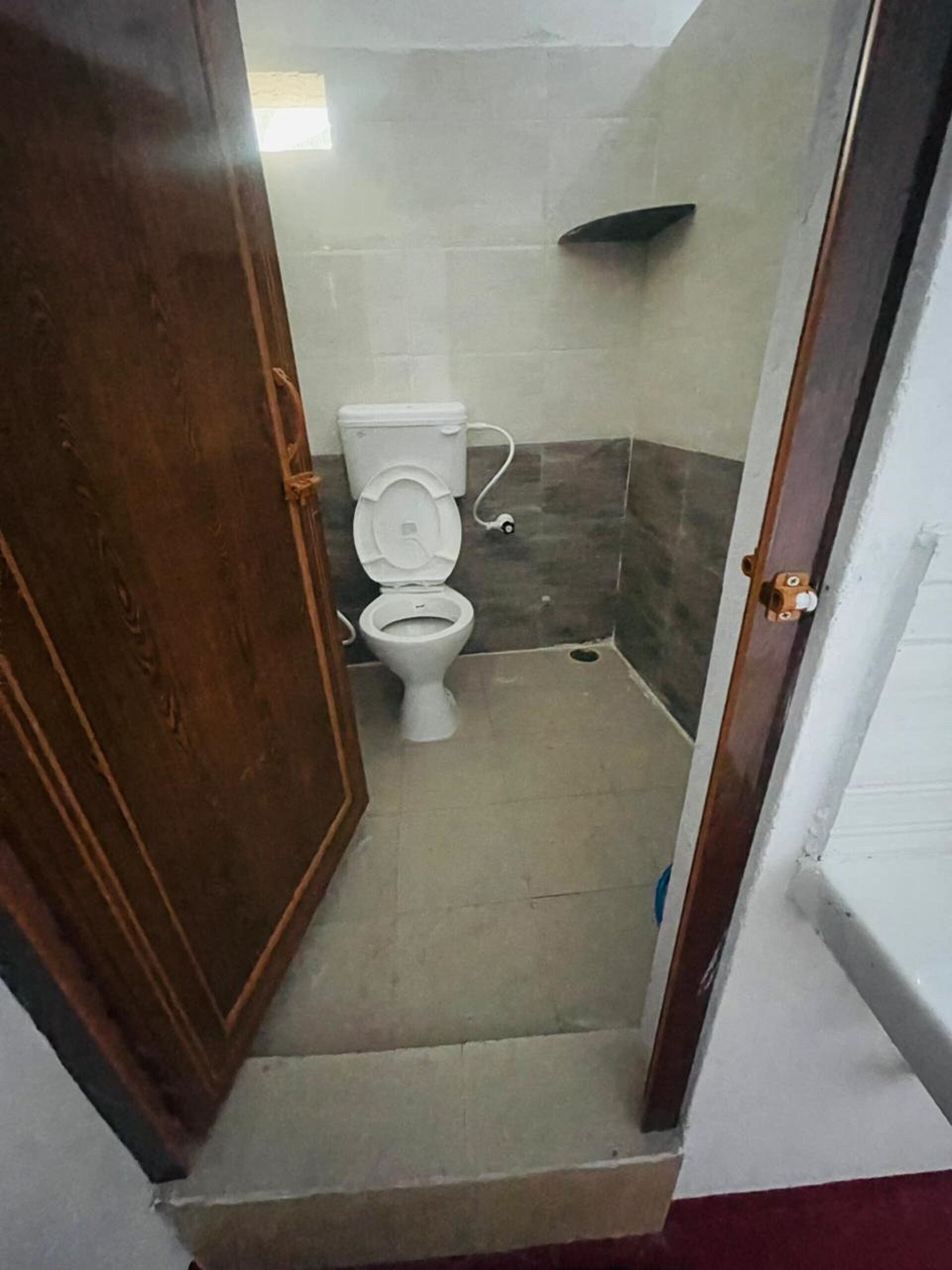 A small, narrow bathroom with a toilet and a shower area.