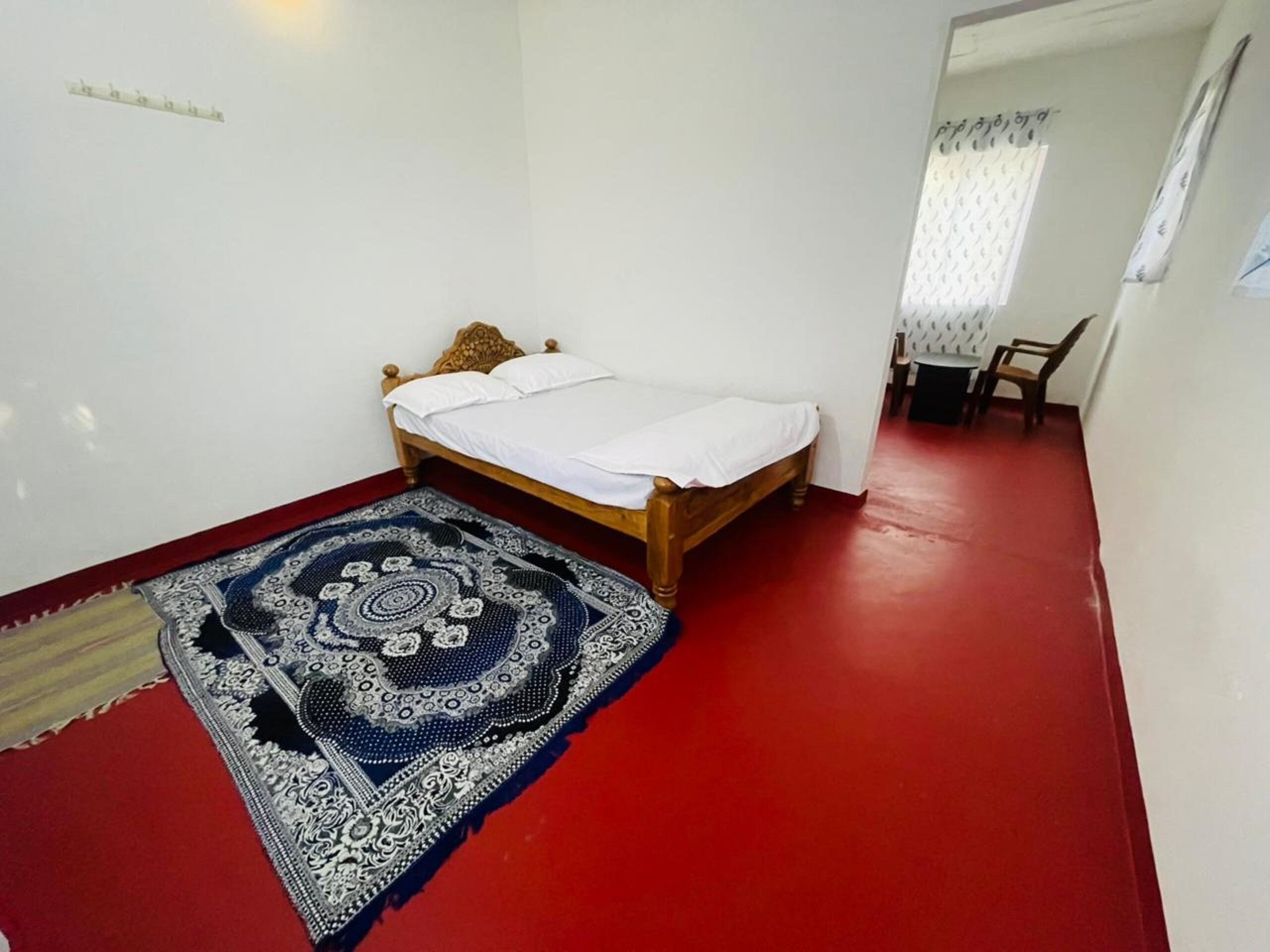 Un dormitorio con una cama de madera, suelo rojo y una alfombra estampada.