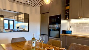 A modern kitchen with a wooden dining table, wine bottle, glasses, and two wooden containers. - Villa Billubium-Authentic Stone Villa with Private Heated Pool (Lokvičići)