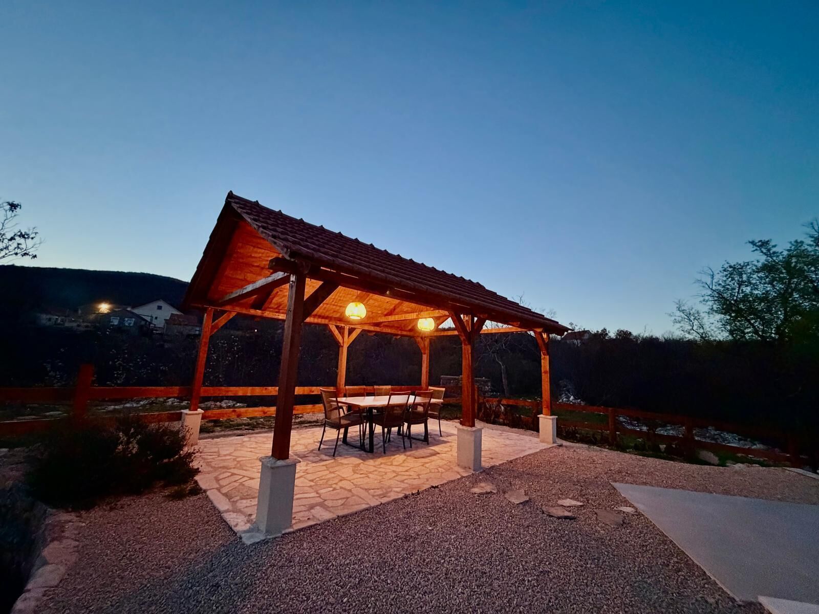 A wooden gazebo with a tiled floor and a table and chairs set up inside.