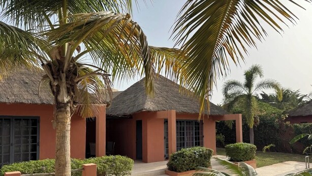 A resort with a pool, palm trees, and a thatched-roof building. - Villa SOPHIA (Ngaparou)
