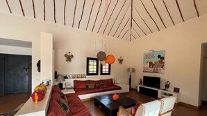 A modern living room with a sofa set, a coffee table, and a TV. There are decorative items on the walls and a door in the background. - Villa SOPHIA (Ngaparou)