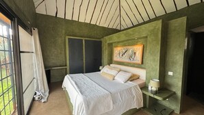 A bedroom with a bed, a nightstand, a painting, and a window. - Villa SOPHIA (Ngaparou)