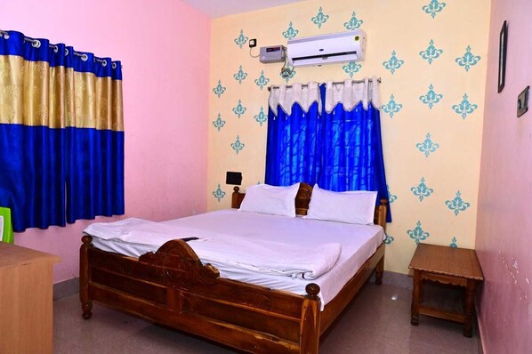 A bedroom with a wooden bed, blue and gold curtains, an air conditioner, and patterned wallpaper. - Kirti Inn Puri (Puri)