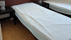 A hotel room with two single beds, a nightstand with a lamp, and a wall-mounted light fixture.