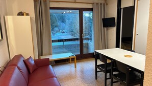 A room with a red leather sofa, a small table, a TV mounted on the wall, and a sliding glass door leading to an outdoor area.