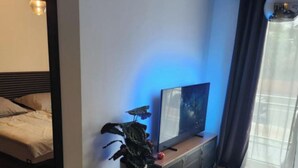 A modern bedroom with a bed, bedside table, a potted plant, a small table with a lamp, and a large window with curtains. - Modern 2-room vacation apartment with balcony and space for up to 4 guests (Bremen)