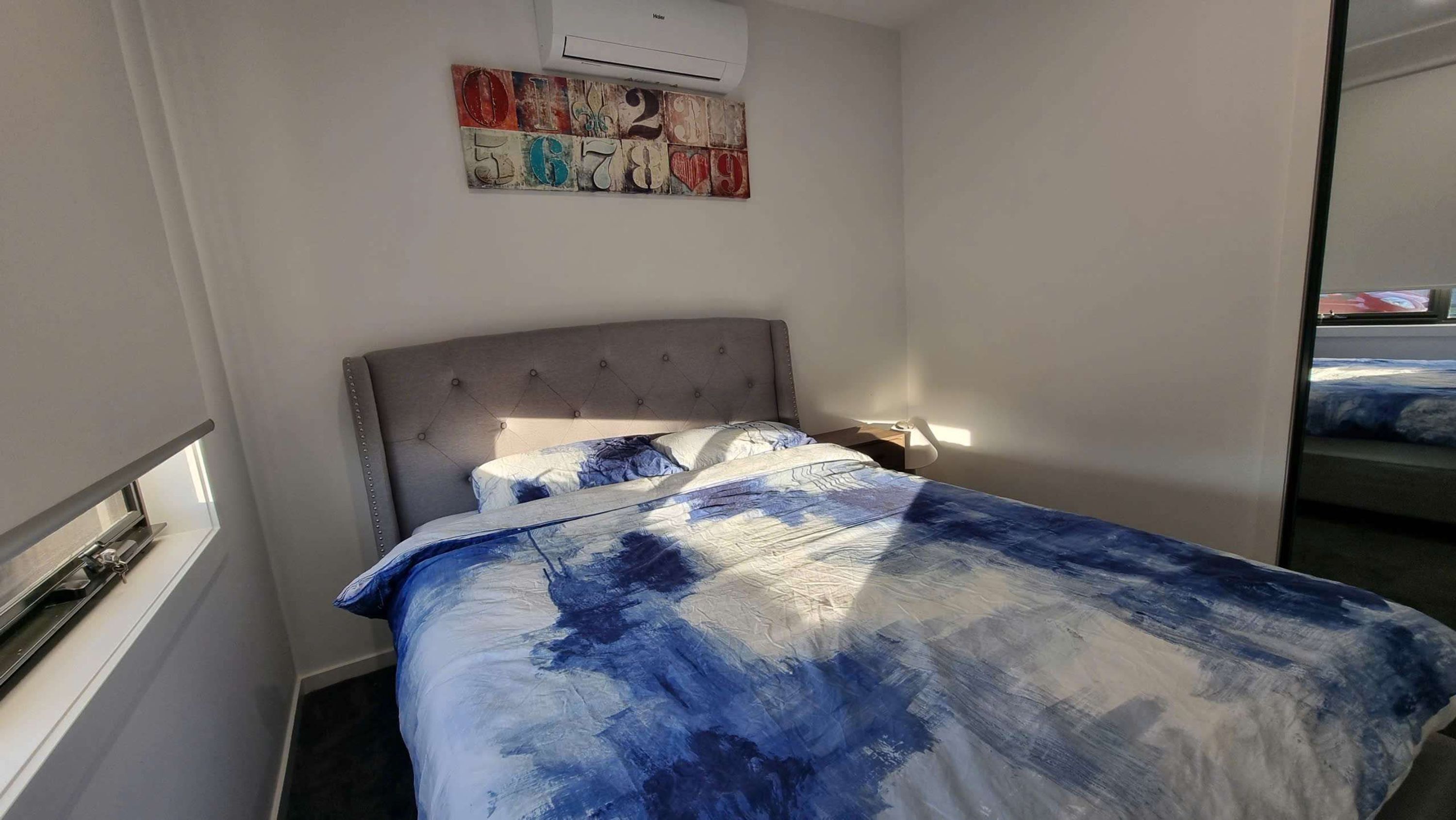 A bedroom with a bed, a headboard, a wall-mounted air conditioner, and a decorative number plaque.