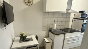 A compact kitchen with white cabinetry, a small dining table, a chair, a microwave, and a clock on the wall.