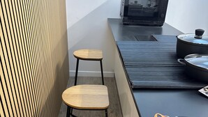 Eine Küchenzeile mit zwei hölzernen Hocker, einer Mikrowelle, einem Wasserkocher und einer Packung Zahnpasta der Marke Total.