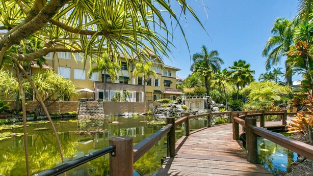 Eine Holzbrücke über einen Teich, im Hintergrund ein Gebäude.