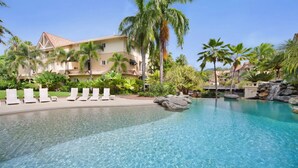 Ein Resort-Pool mit klarem Wasser, umgeben von Palmen und Liegestühlen.