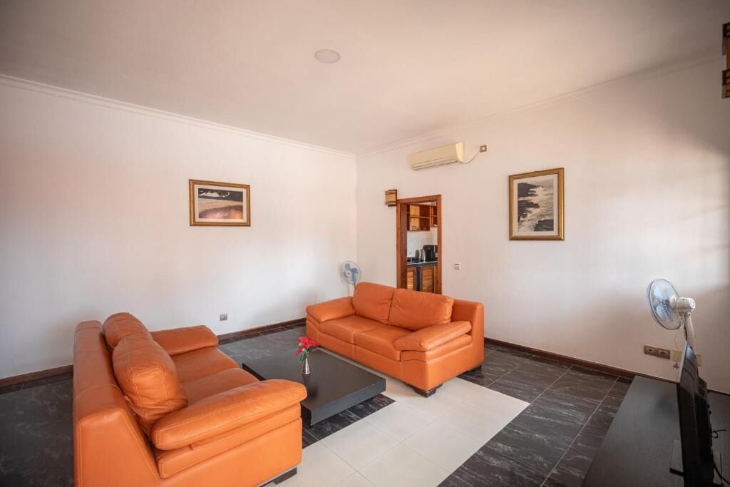 Una sala de estar con dos sofás naranjas, una mesa de centro y un ventilador.
