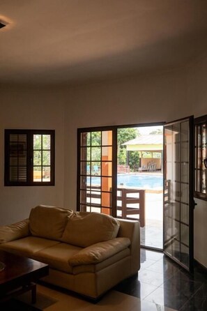 Habitación con sofá, una mesa y un ventanal corredizo que da a un área exterior con piscina.