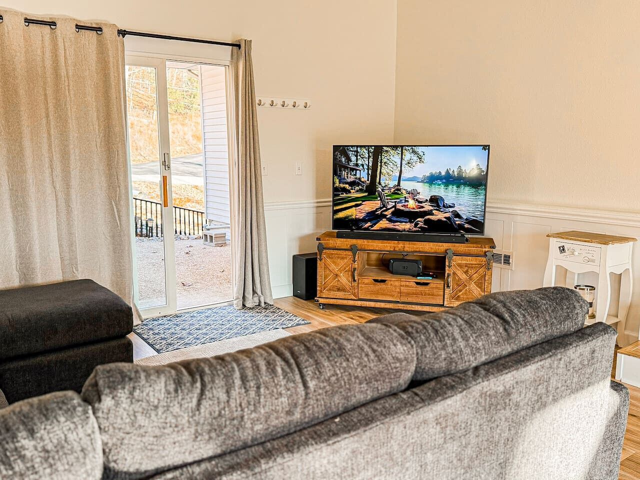 Ein Wohnzimmer mit grauem Sofa, einer Holzeinrichtungsanlage mit Fernseher und einer Glasschiebetür, die zu einem Außenbereich führt.
