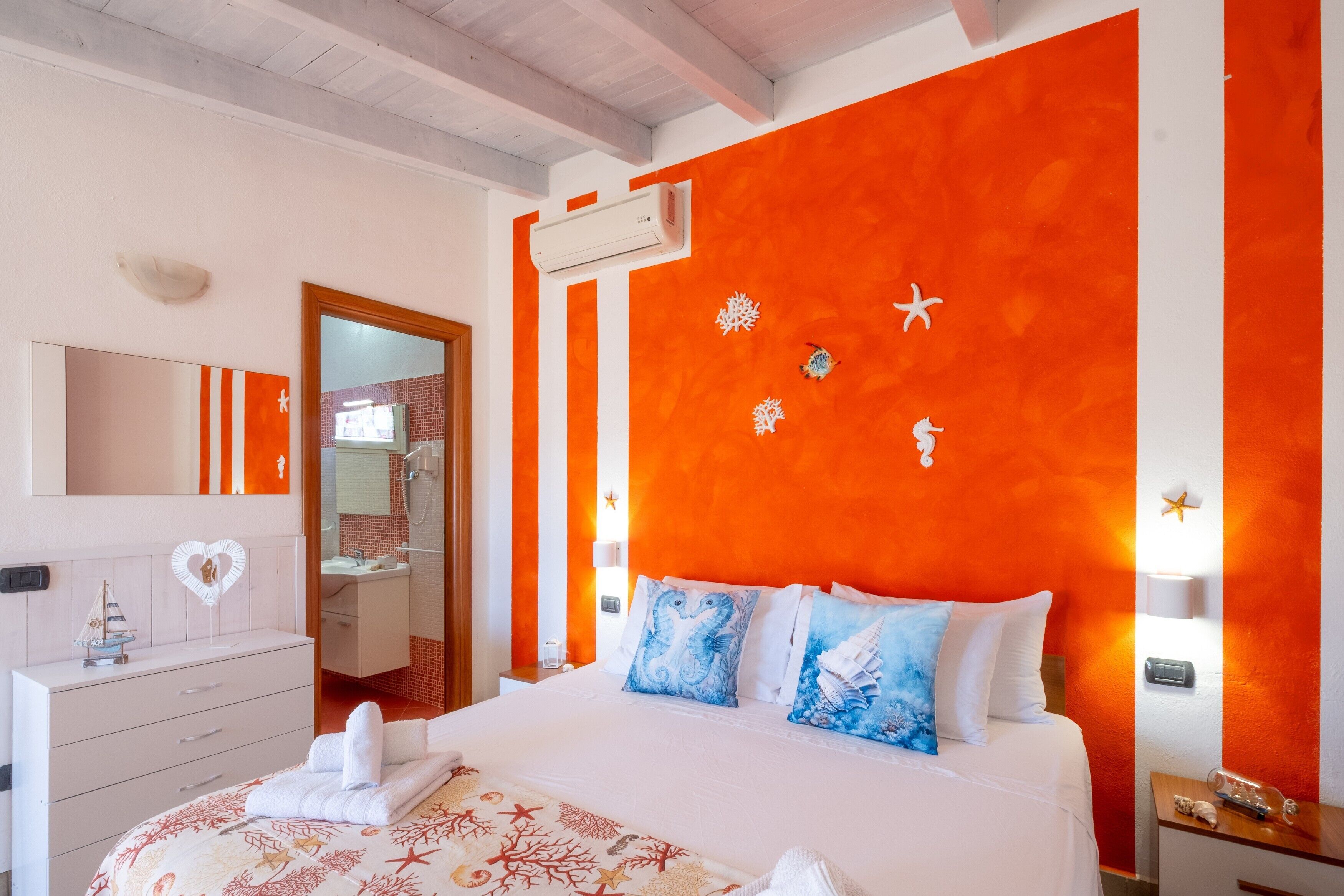 A hotel room with a large bed, a dresser, a mirror, and an orange accent wall.