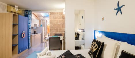 A hotel room with a bed, a desk, a chair, a bathroom, and a kitchenette.